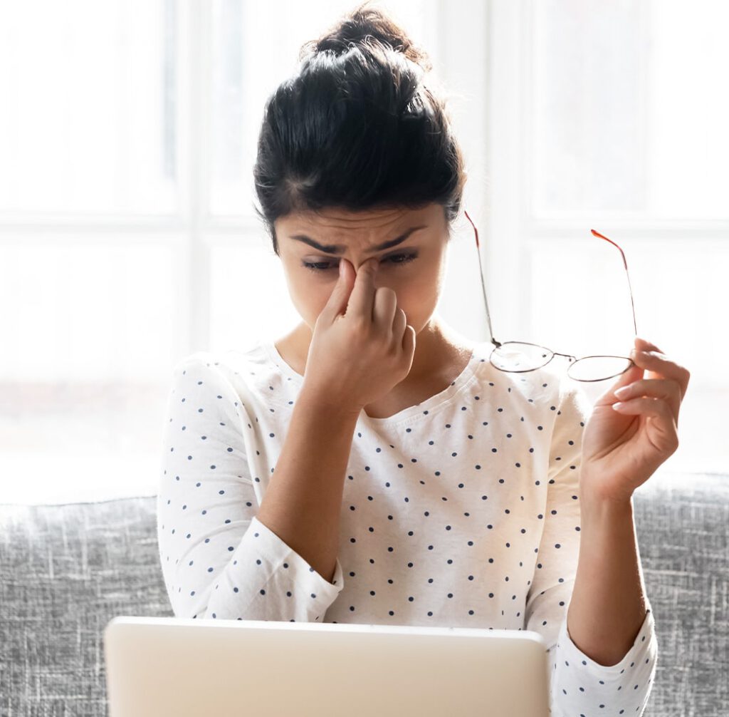 A woman taking off her glasses and rubbing the bridge of her nose due to digital eye strain pain