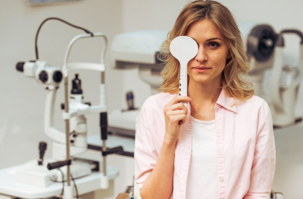 A woman is sitting on a chair while covering her right eye while looking at a chart in a distance