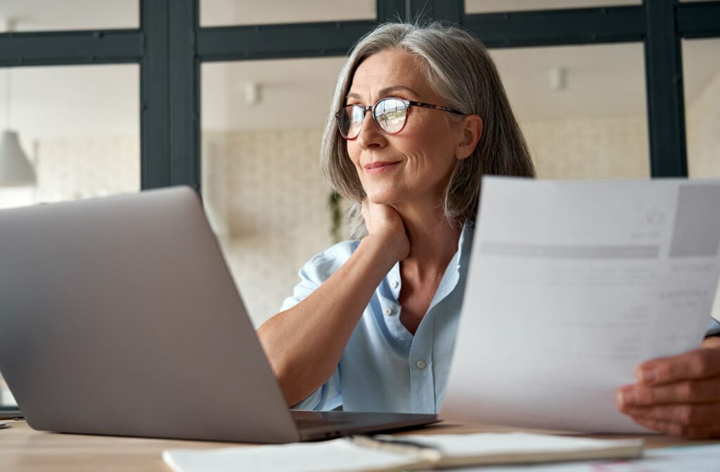 A middle-aged woman wearing glasses works at her laptop