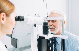 A female optometrist examines an older man's eyes to check for certain conditions like diabetes.