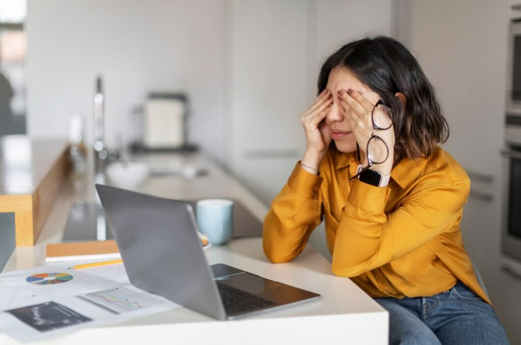 A person sitting at the computer struggling from a headache caused by dry eyes