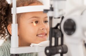 A child smiling during a slit-lamp eye exam to find out if their myopia has gotten worse.