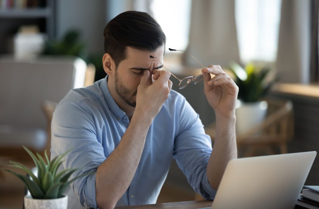 A young adult working at their laptop, rubbing their eyes in frustration due to eye strain.