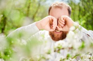 Man rubbing irritated eyes outdoors during spring allergy season