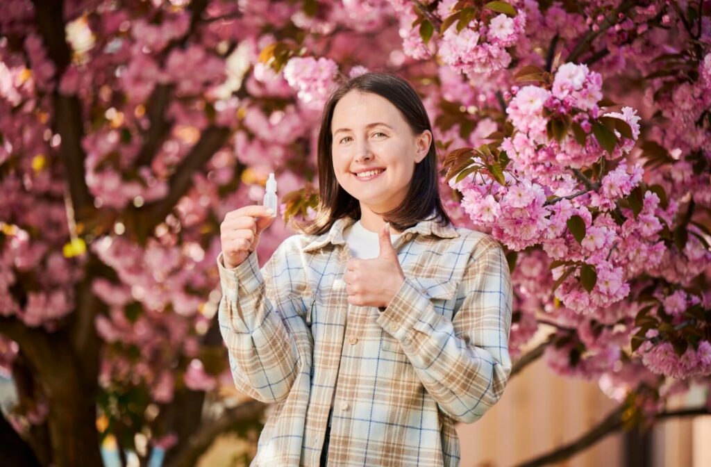 Smiling woman holding eye drops with blooming trees in the background