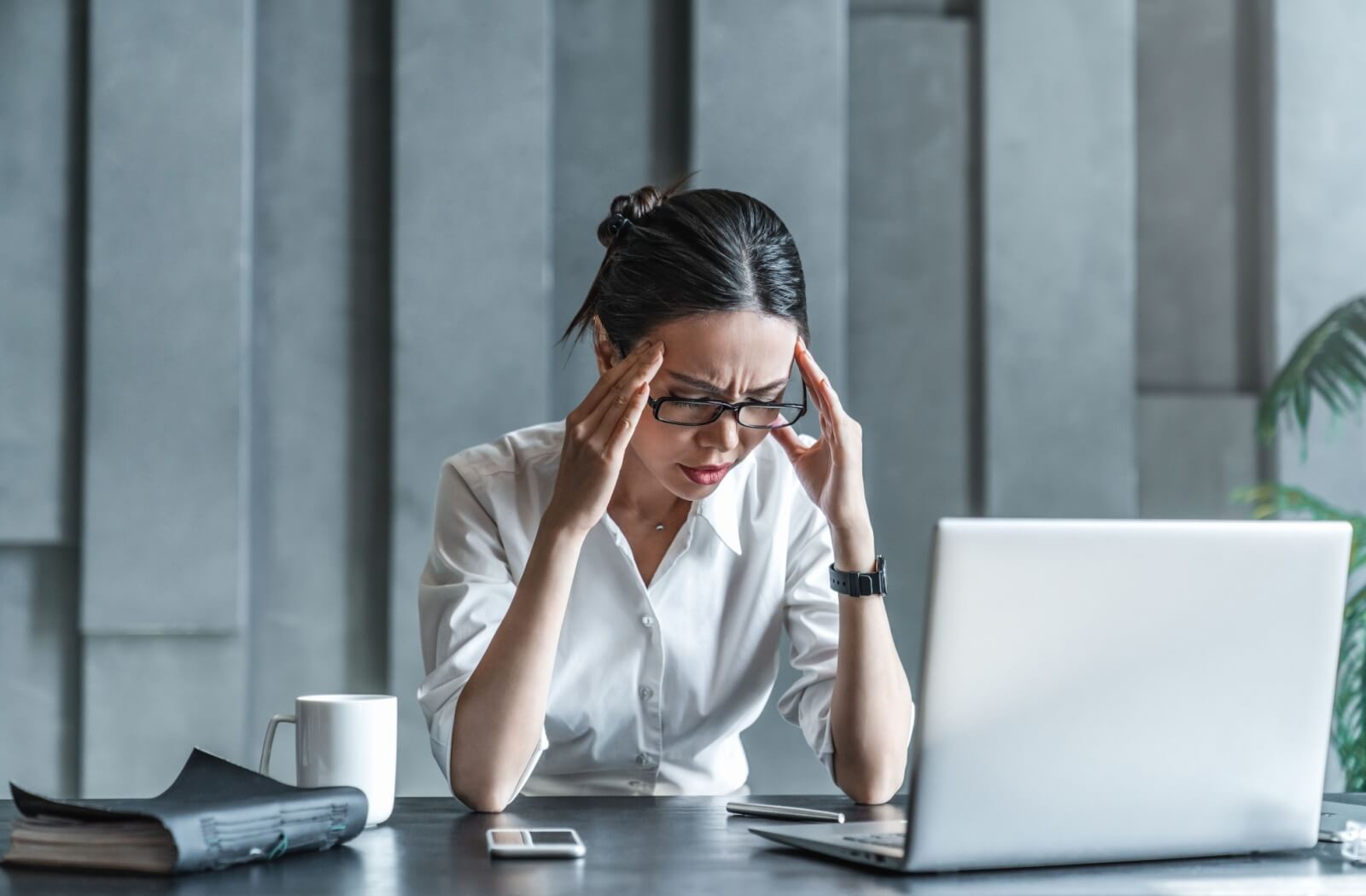 Someone working on a computer deals with a headache by rubbing their temples.