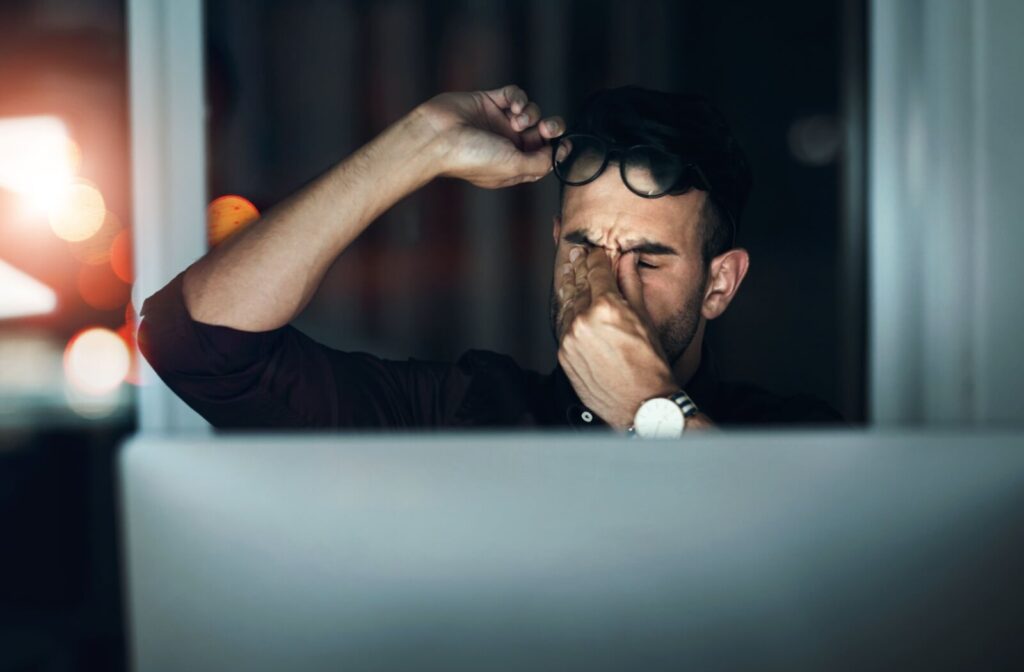 Someone working on a computer late a night removes their glasses and rubs their eyes.