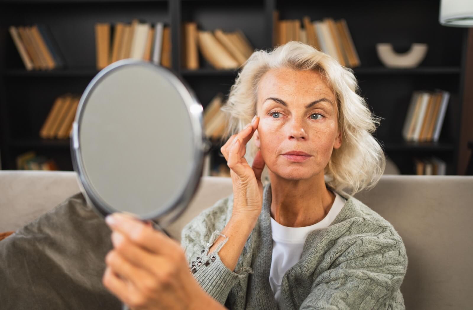 Person examining facial wrinkles in mirror at home considering IPL treatment.