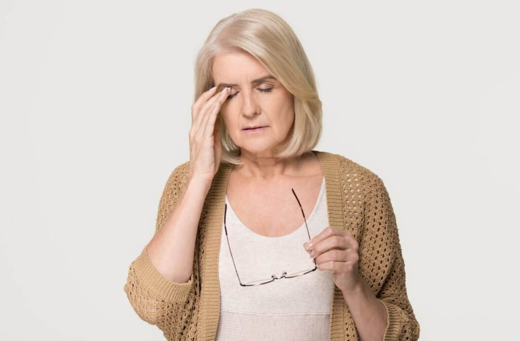 Older person with possible macular degeneration holding glasses and touching her eye.