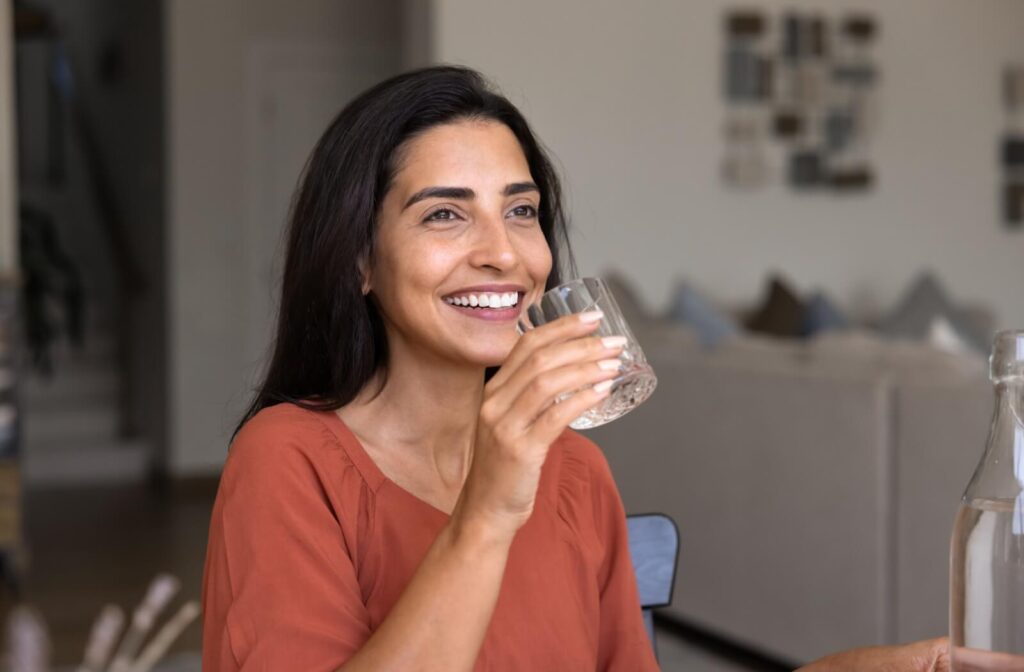 A smiling individual holding a glass of water, illustrating hydration as part of dry eye management.