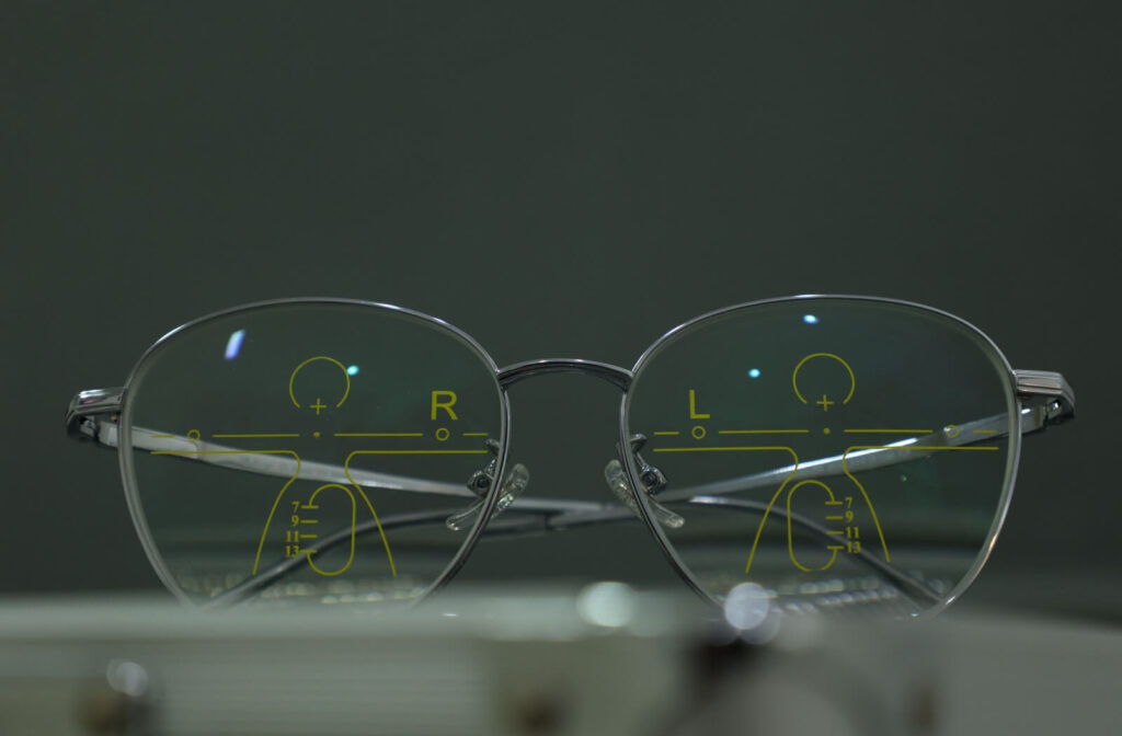 A close-up of progressive lenses in silver frames featuring yellow optical alignment markings for precise vision correction.